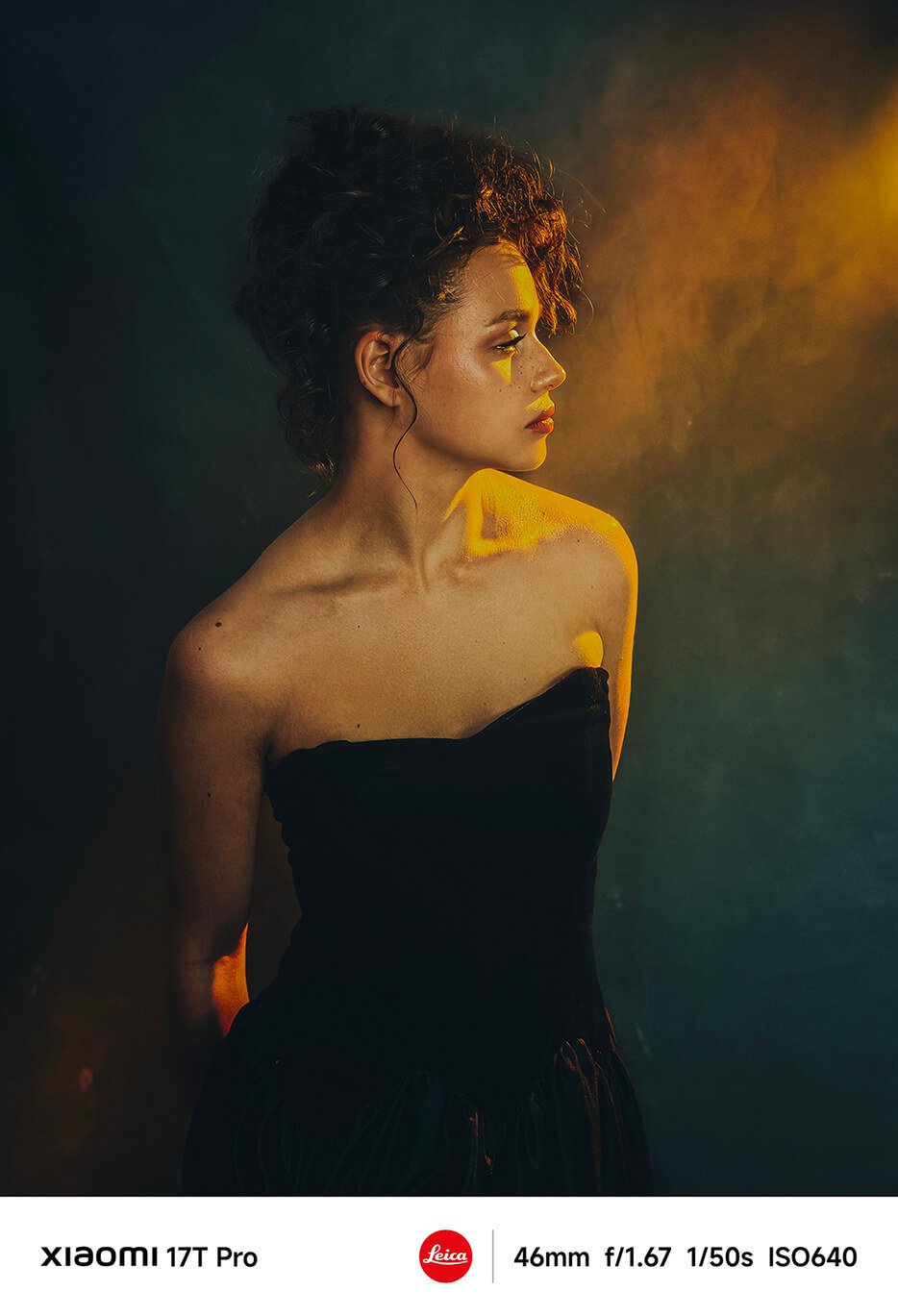 Femeia stă în profil, purtând o ținută fără mâneci de culoare neagră, iar fundalul este un gradient de culori blânde, creând o atmosferă artistică.