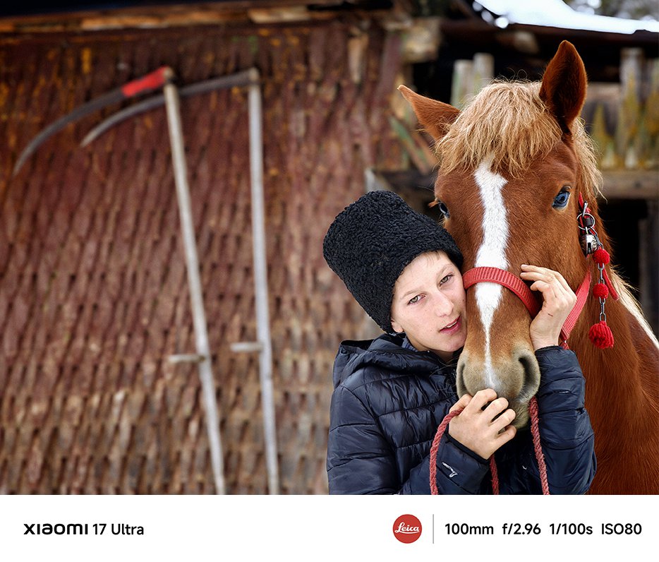 O persoană îmbrățișează un cal, iar fundalul este o fermă din lemn.