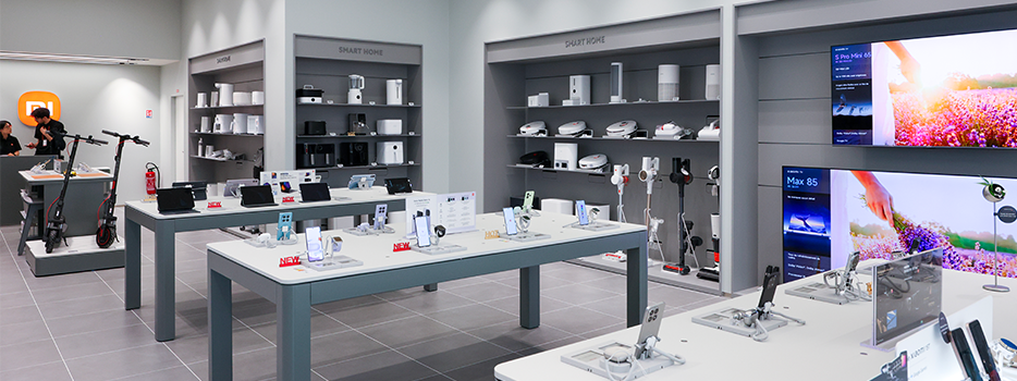 Intérieur d'un magasin de vente au détail d'électronique moderne, présentant plusieurs modèles de smartphones, d'appareils domestiques et de voitures électriques, les produits étant soigneusement disposés sur des tables et des étagères, avec un fond de murs minimalistes et d'écrans d'affichage.