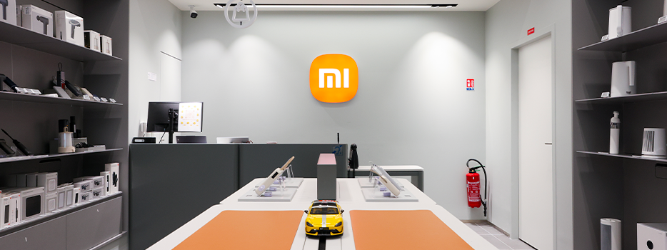Dans le magasin Xiaomi, divers produits électroniques sont exposés, une voiture miniature se trouve au centre et le logo Xiaomi est accroché au mur.