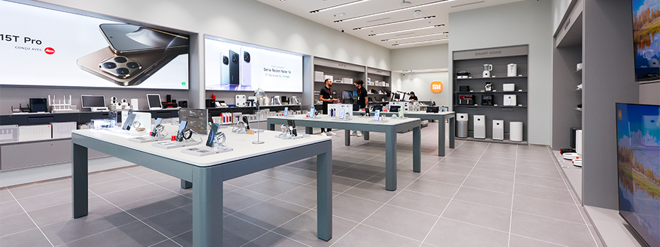 L'intérieur d'un magasin d'électronique moderne, présentant divers appareils électroniques et accessoires, des clients examinant les produits, un grand écran publicitaire sur le mur.